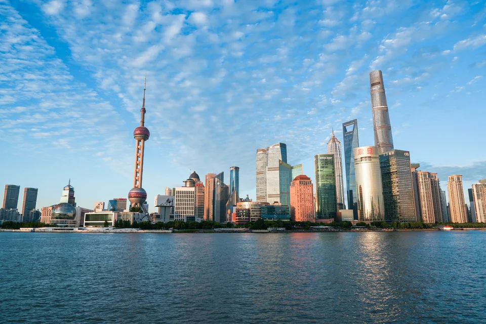 隔着宽阔的江面望向城市天际线，蓝天下，船只从水面经过。